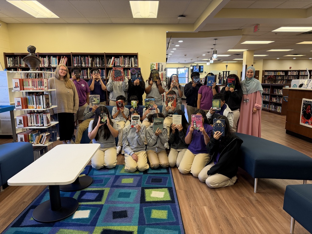 From left to right: the library media specialist, Mrs. Scheerer, students from Ms. Aquino's classroom with their book choices covering their faces,  and Ms. Aquino standing to the right