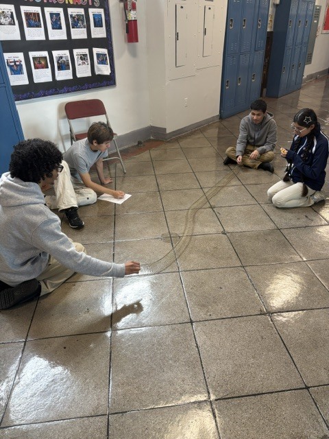 Image of four students using Slinkies in the school hallway to demonstrate wave behavior in order to learn about seismic waves that cause earthquakes as a Physics class activity.   Imagen de cuatro estudiantes utilizando resortes tipo Slinky en el pasillo de la escuela para demostrar el comportamiento de las ondas, como parte de una actividad de la clase de física,  y así aprender sobre las ondas sísmicas que provocan terremotos