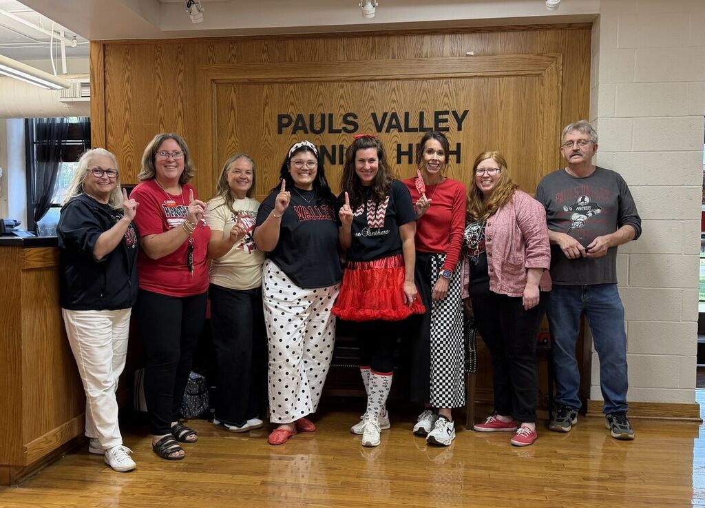 Nine PVJH staff members pose in the school lobby wearing red, black, and Panther-themed clothing for an undercover Panther Pride dress-up day.