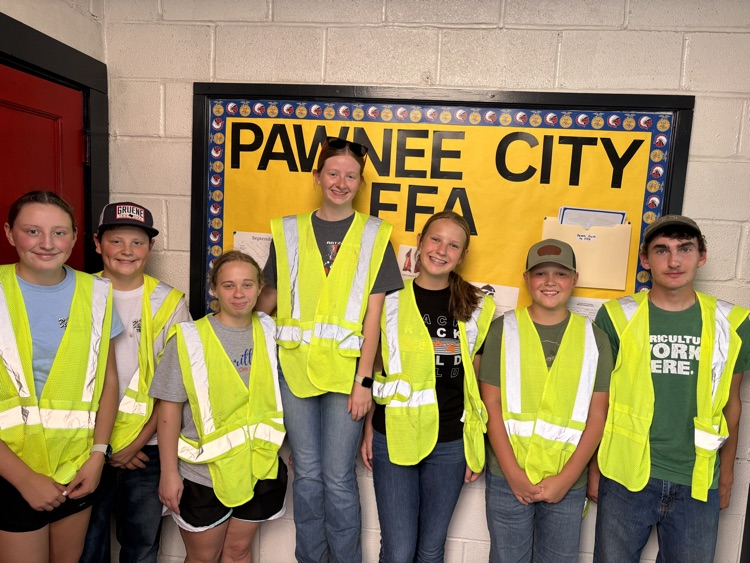 7 students in high visibility vests standing in front of the Pawnee City FFA bulletin board