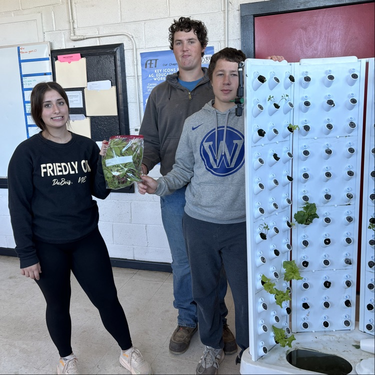 Morgann, Aidan, and Braydon holding up a bag of produce, standing next to the grow tower  