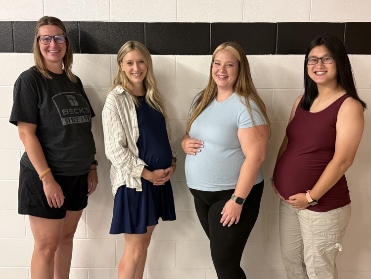 four women standing against a white wall