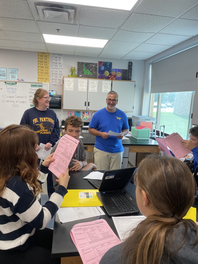 Mr. Didier and Ms. Manley smiling with students around a table