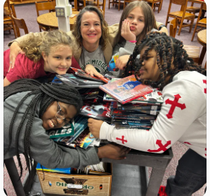 Students and their librarian hug a pile of books. 