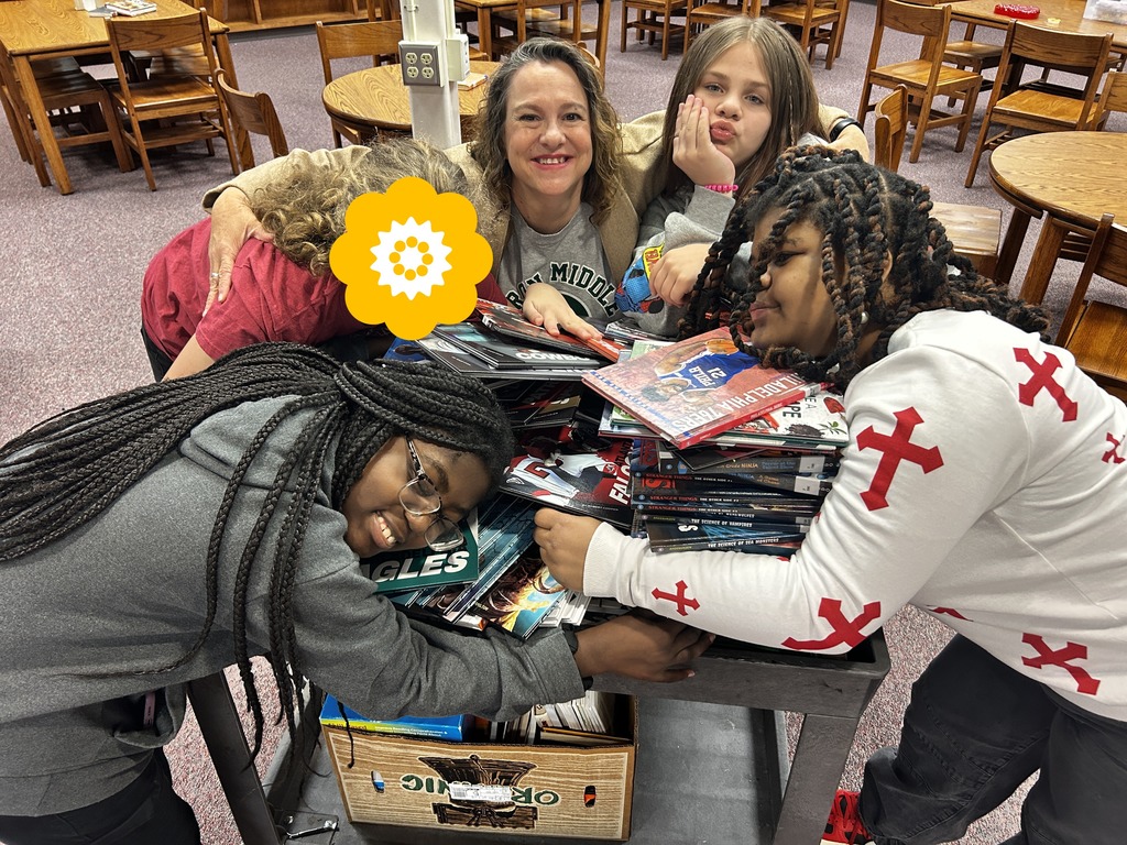 Students and their librarian hug a pile of books. 