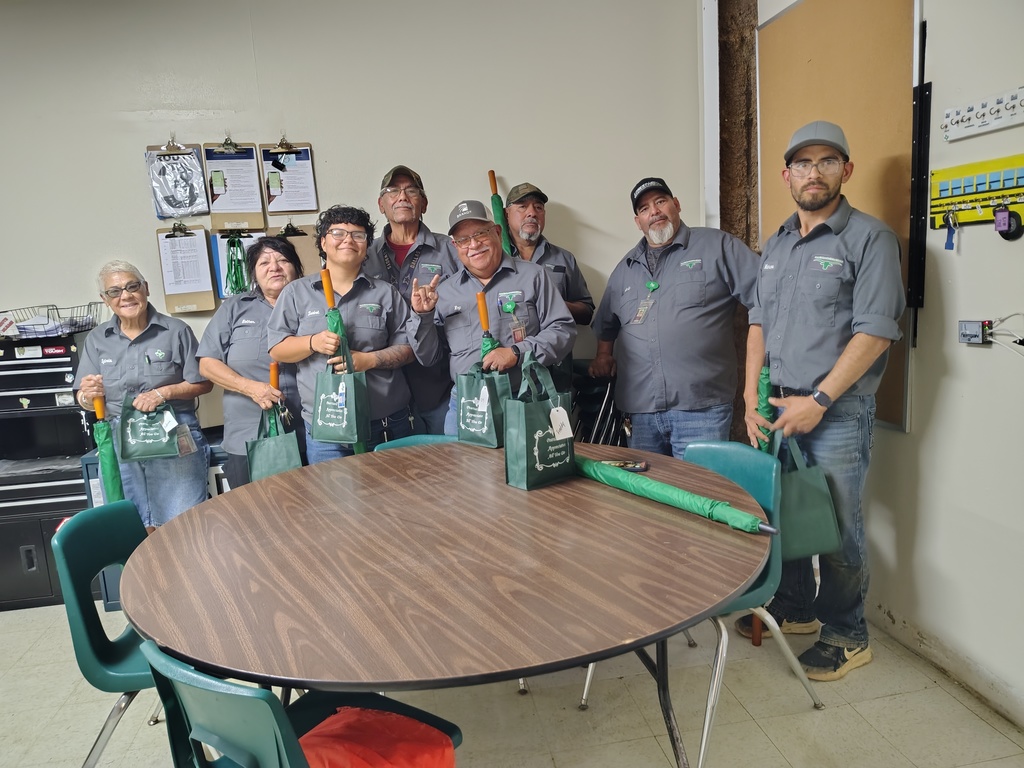 Group photo of the Pearsall ISD maintenance department in a office breakroom with a round table in the foreground 