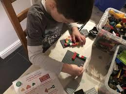 A little boy sitting at a desk playing with Lego blocks