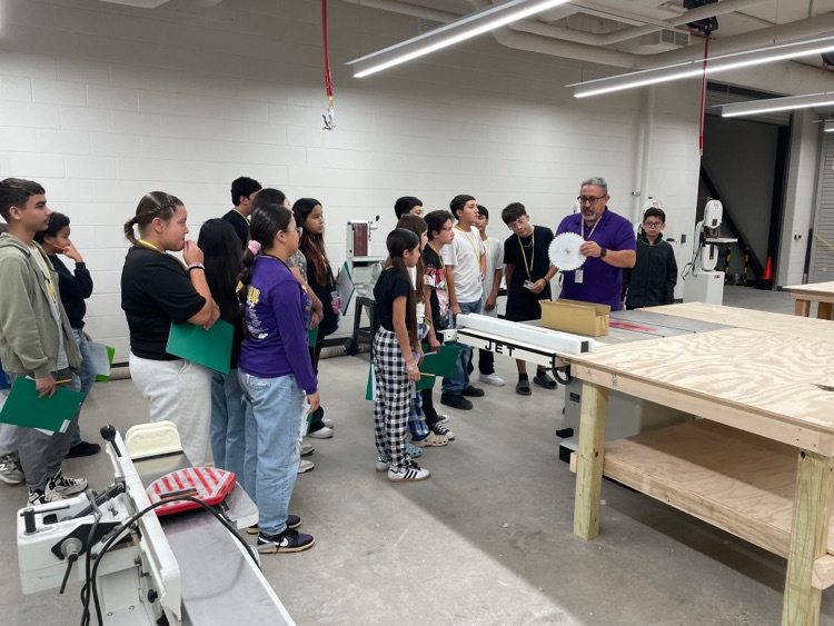 Students are inside of the construction classroom, paying attention to what the teacher has to say about the program. The students are attentive to the teacher.