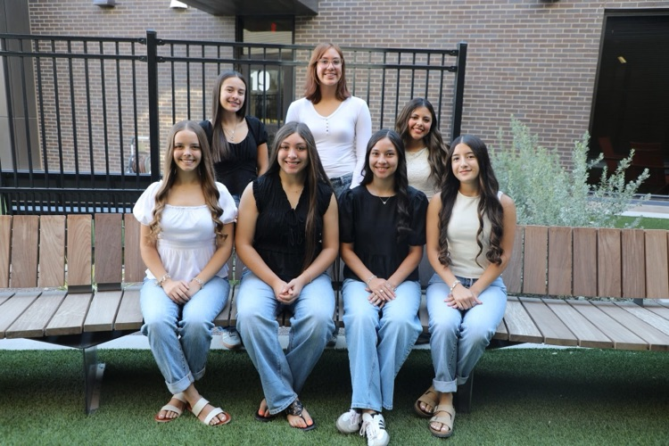 2025 Homecoming Court Girls. Front girls are sitting side by side wearing light blue jeans with dressy tops. Back row girls are standing behind with dressy tops. 