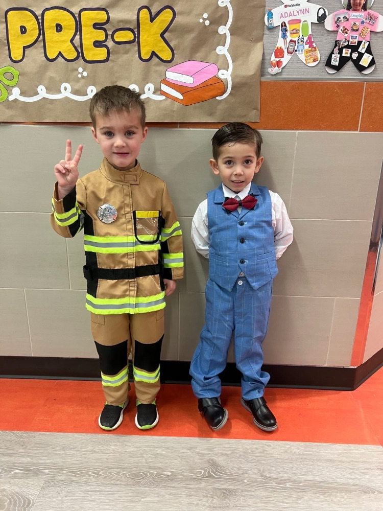 Two boy students pictured as a firefighter and a smart fellow. The firefighter student has his hand up in a peace sign while the other student has his hands behind his back.
