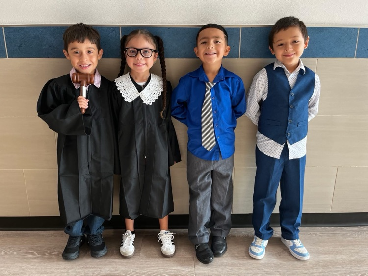 Four students aligned on the wall dressed up. They are seen dressing up with outfits that consists of dresses, and polos with ties.