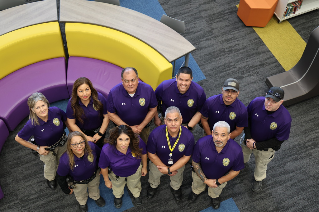 PBTISD Police in purple shirts, some seated and some standing, posing together in what appears to be a learning or community space with play equipment.