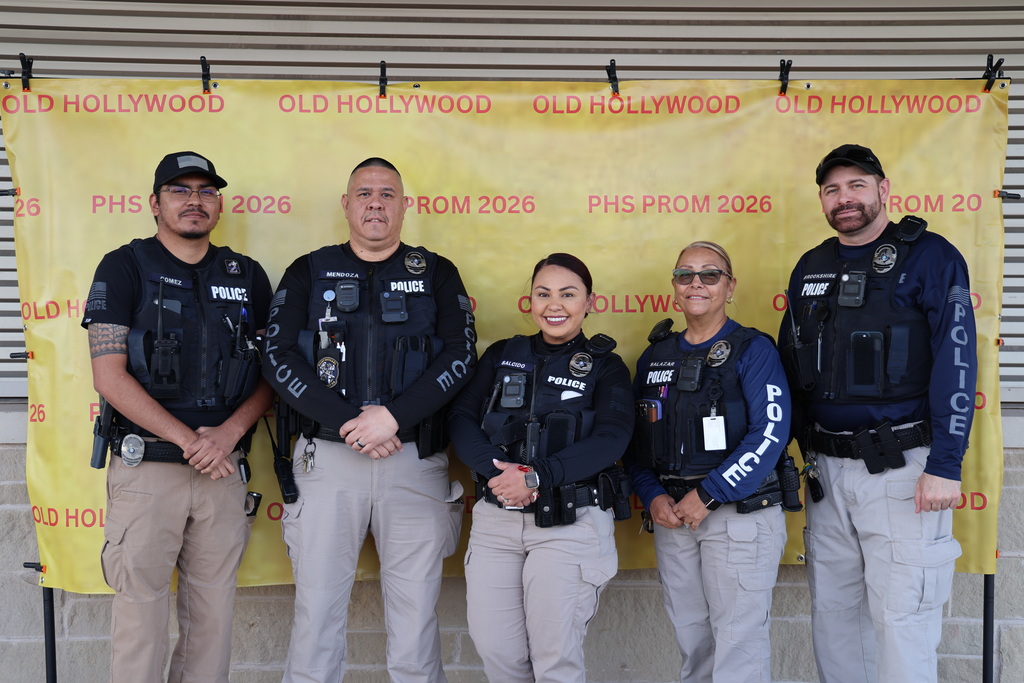 A group photo of several law enforcement officers dressed in uniform, standing in front of signs that say "OLD HOLLYWOOD" and "PHS PROM 2026".