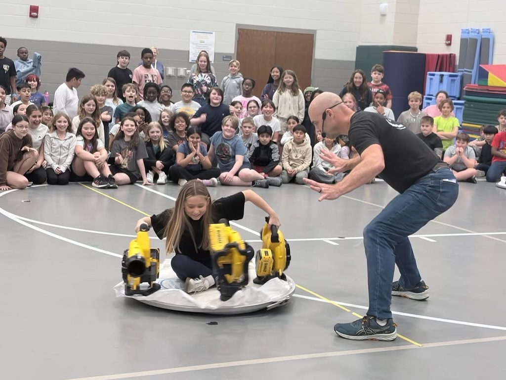 A student on the hovercraft with the instructor talking to them.  The other 5th grade students are watching!