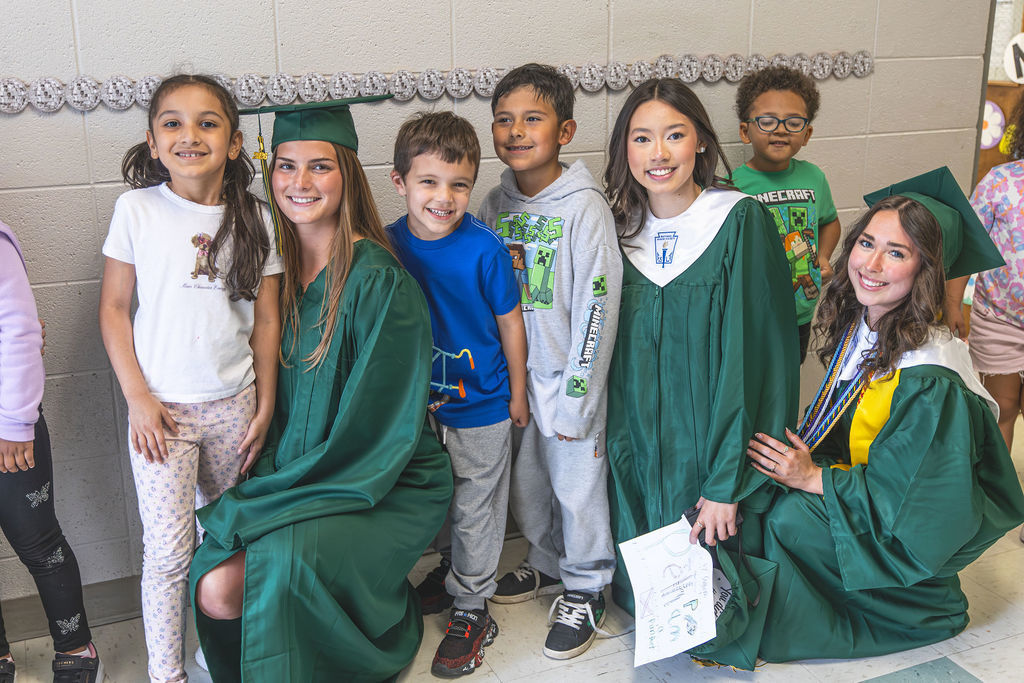 Senior students in cap and gown with several elementary students
