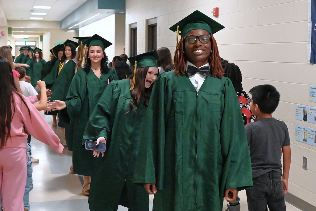 Smiling senior with cap and gown on leading the line of students in a hallway