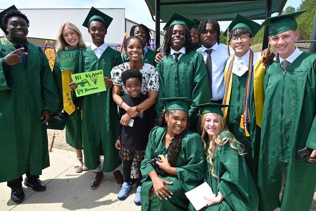 Senior students with green gowns and caps on smiling around school principal