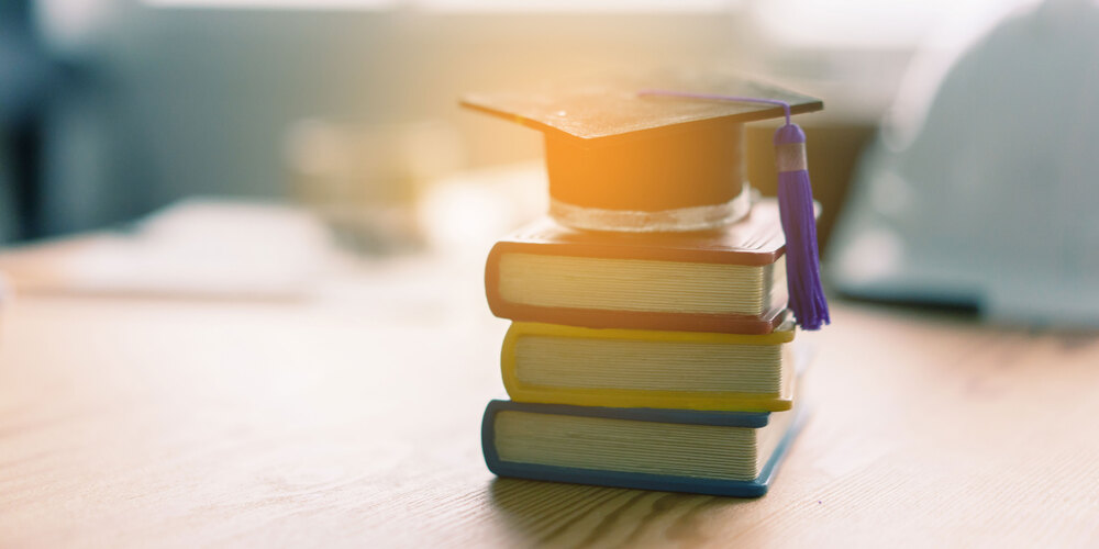 stack of three books on a table with a graduation cap on top