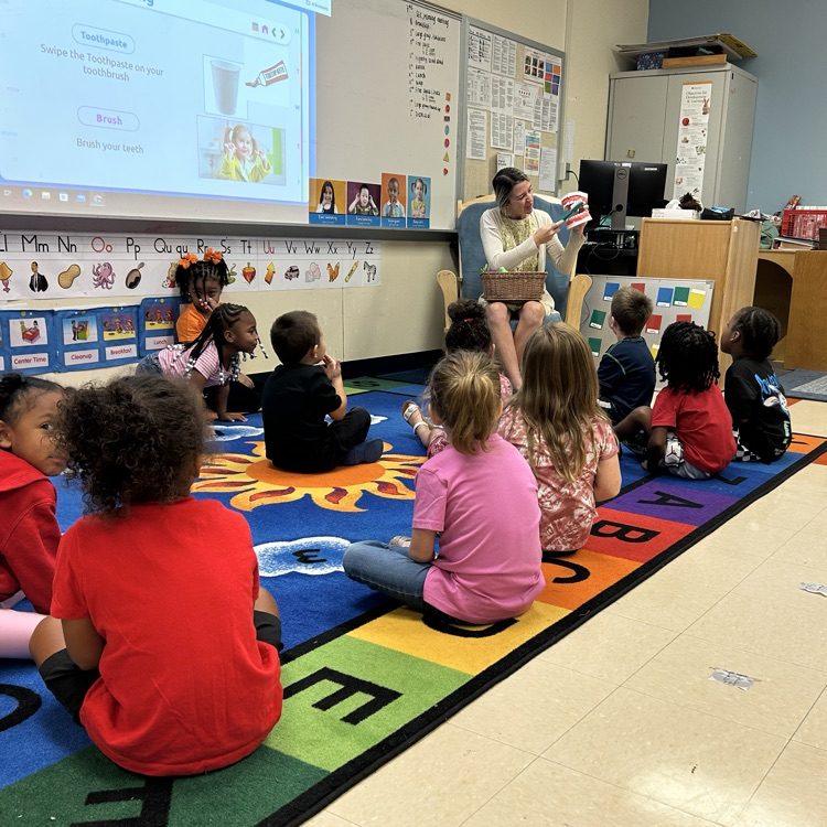 children sitting on rug watching teacher demonstrate toothbrushing
