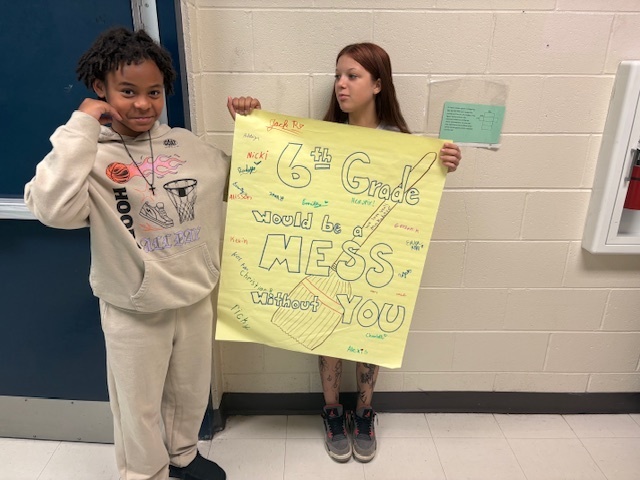 Students holding a sign saying, "6th Grade would be a mess without you."