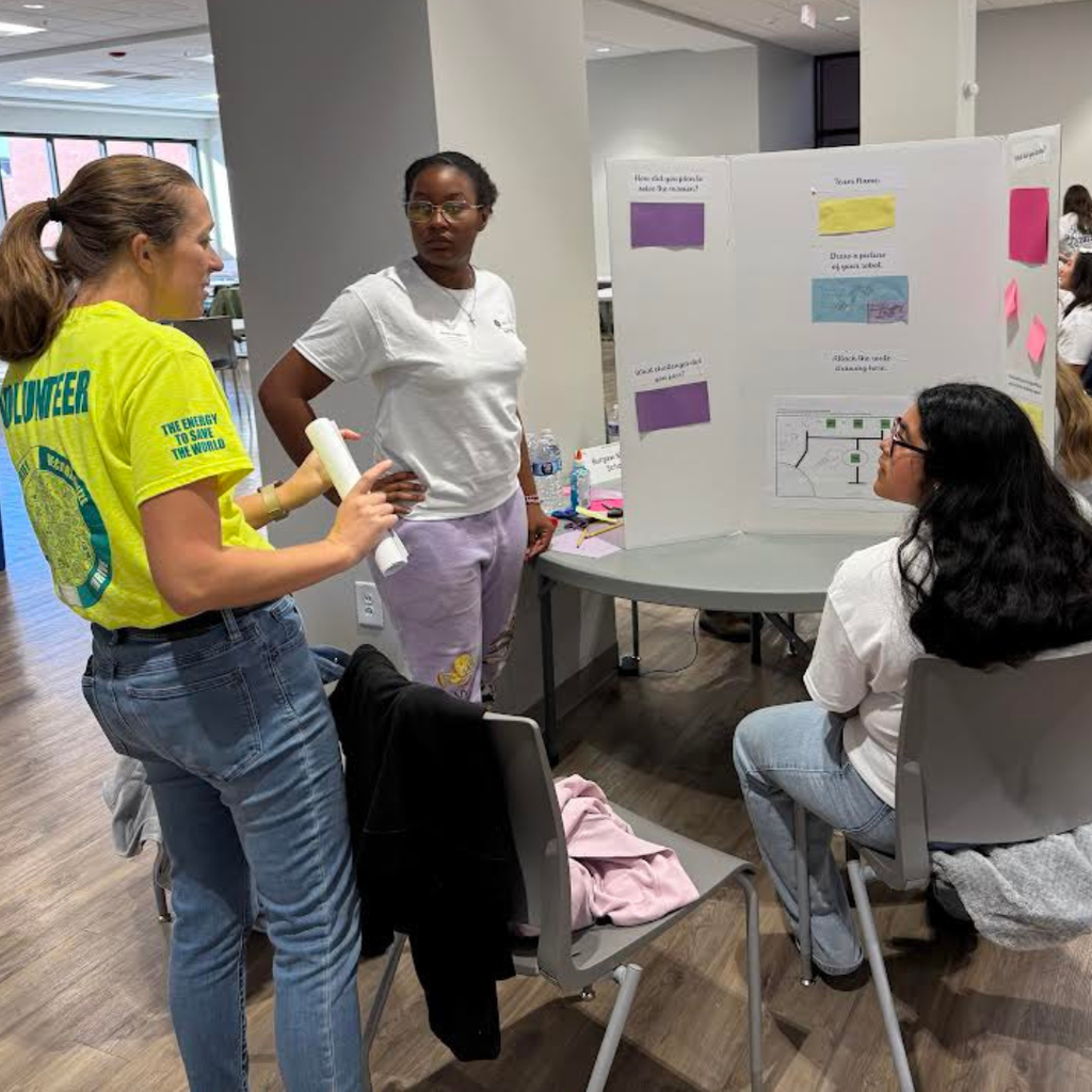 girls in technology group at table with poster board and instructor