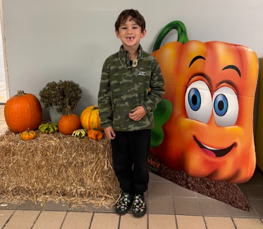student standing by a hay bail with pumpkins