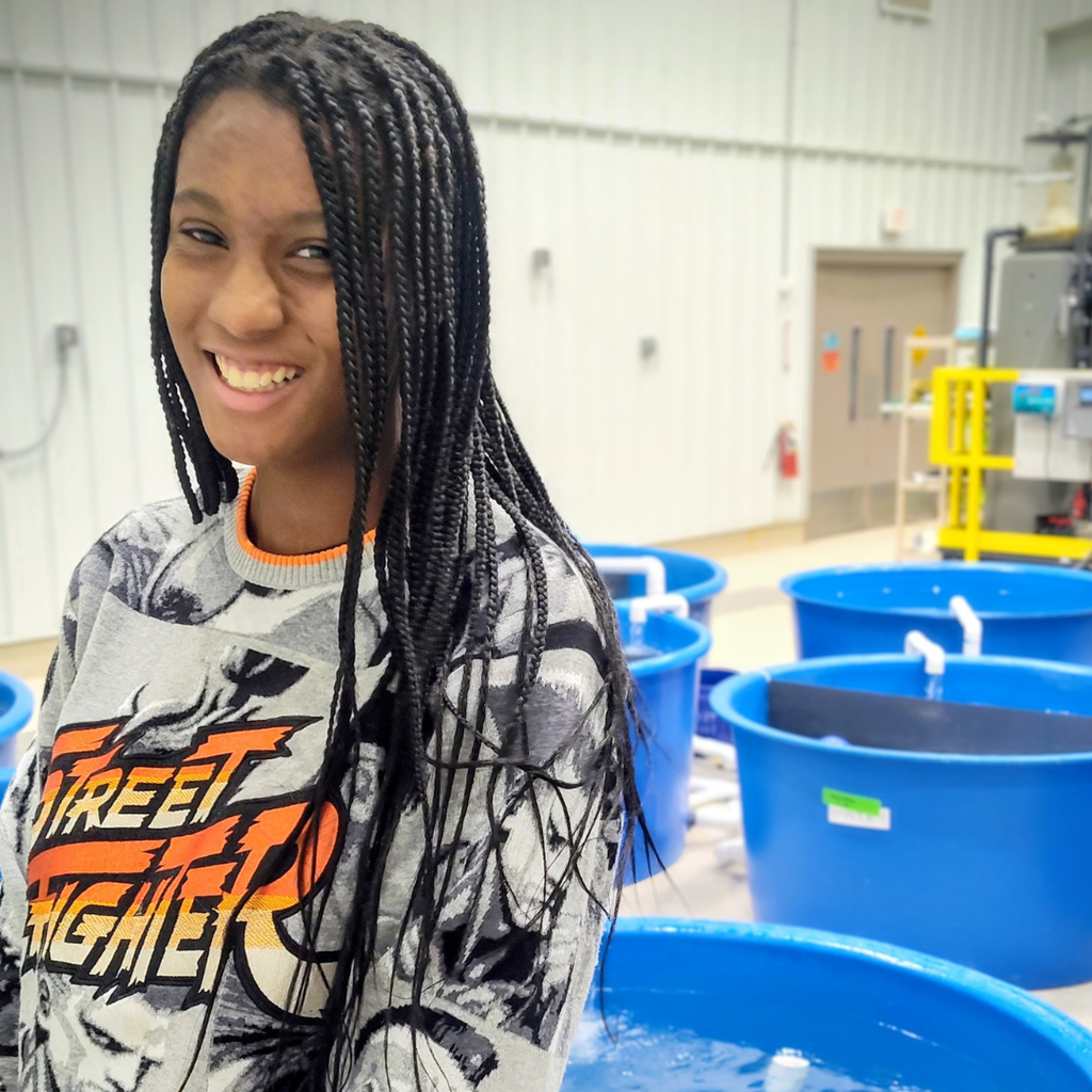 student posing in front of blue bins filled with water