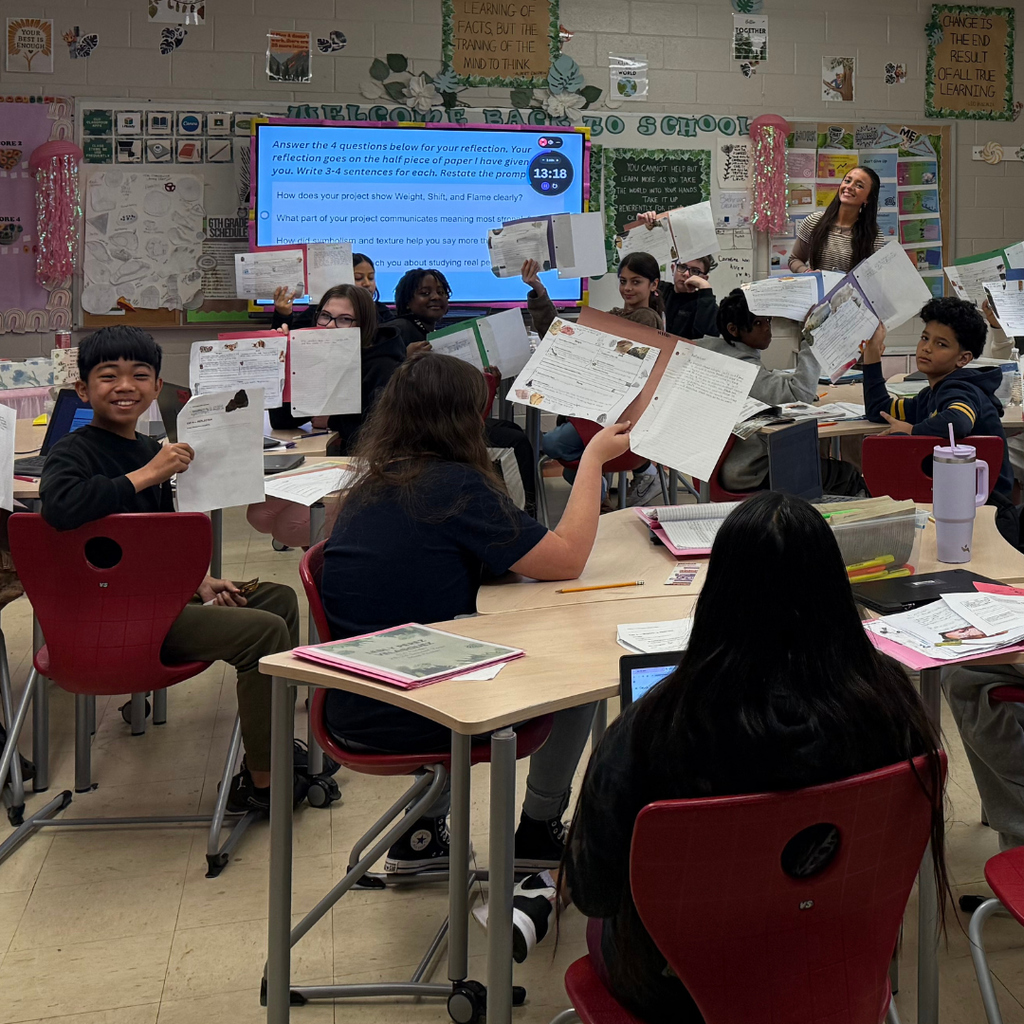 students holding up work with teacher smiling in background