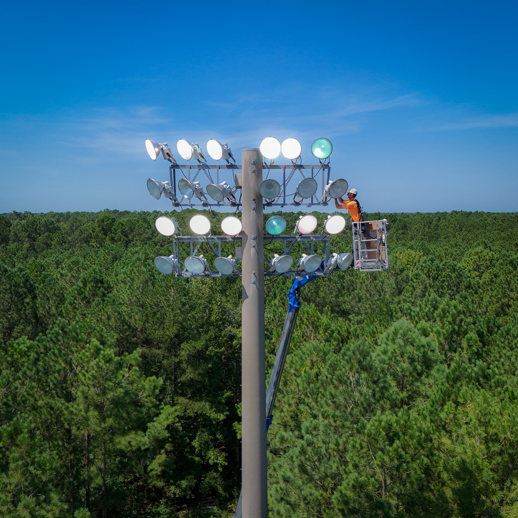 worker installing lights at the football field at heide trask high school