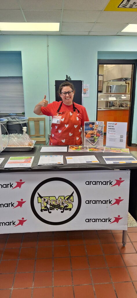 Kitchen staff stands at welcome table for open house to display child nutrition information to parents and incoming students 