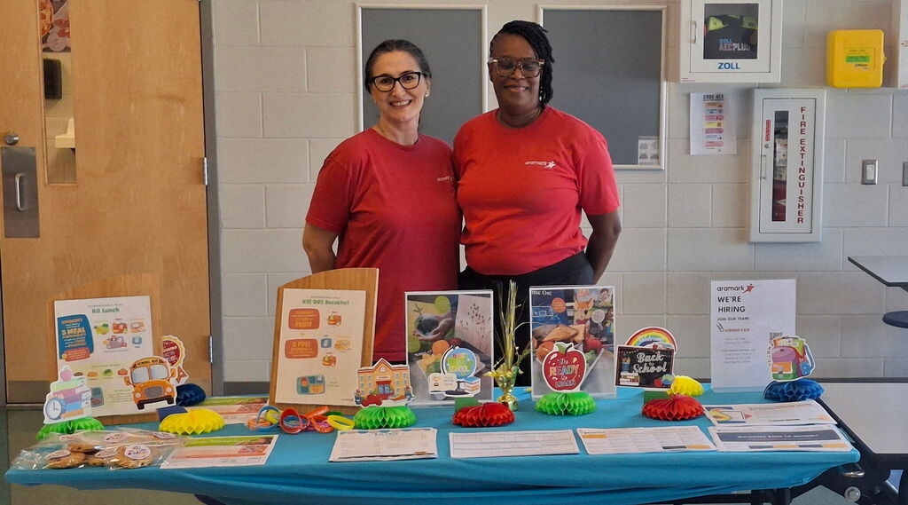 Kitchen staff stands at welcome table for open house to display child nutrition information to parents and incoming students 
