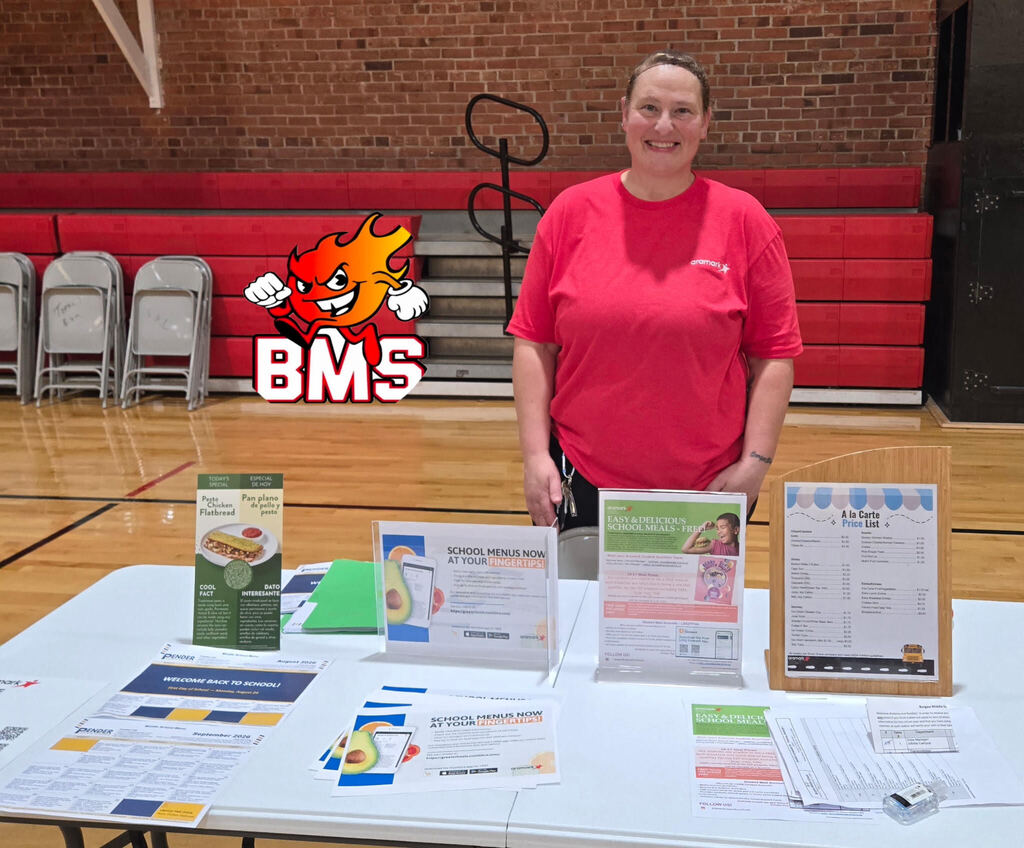 Kitchen staff stands at welcome table for open house to display child nutrition information to parents and incoming students