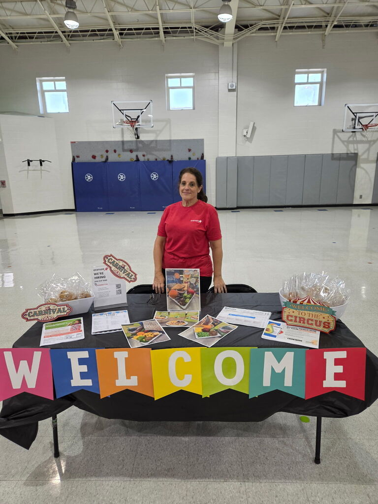 Kitchen staff stands at welcome table for open house to display child nutrition information to parents and incoming students