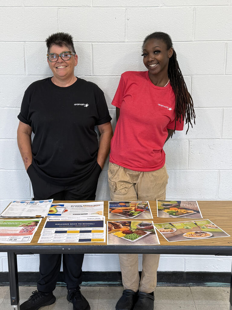 Kitchen staff stands at welcome table for open house to display child nutrition information to parents and incoming students