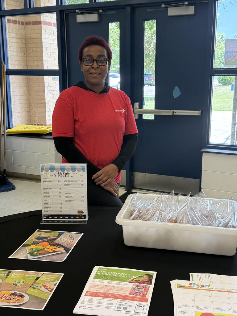 Kitchen staff stands at welcome table for open house to display child nutrition information to parents and incoming students