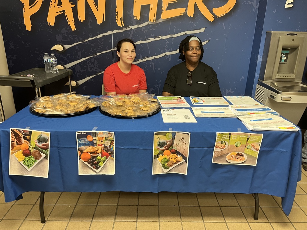 Kitchen staff sits at welcome table for open house to display child nutrition information to parents and incoming students
