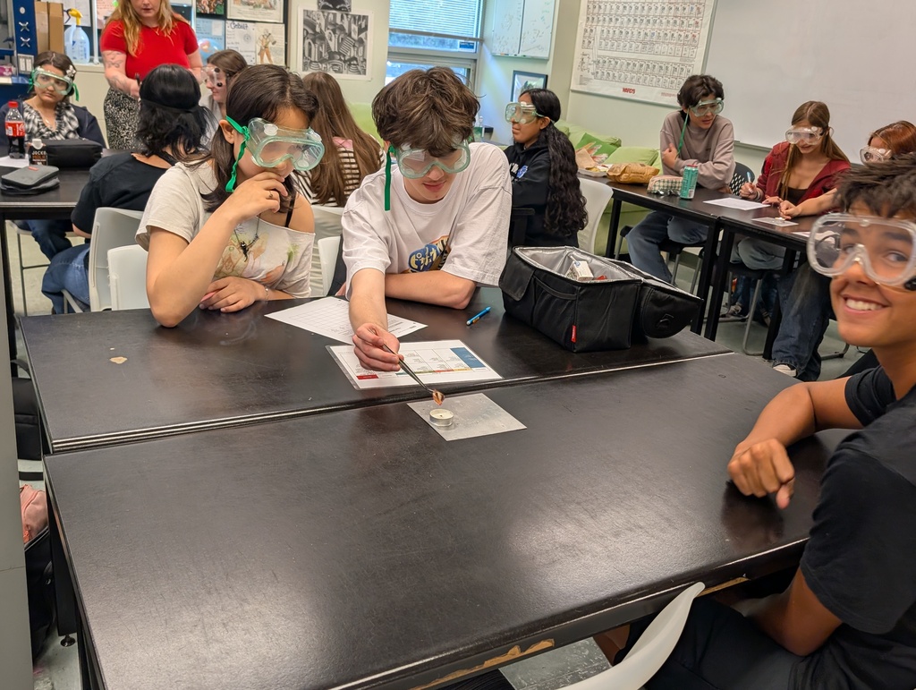Student holding textile sample over candle while group mate smiles at camera