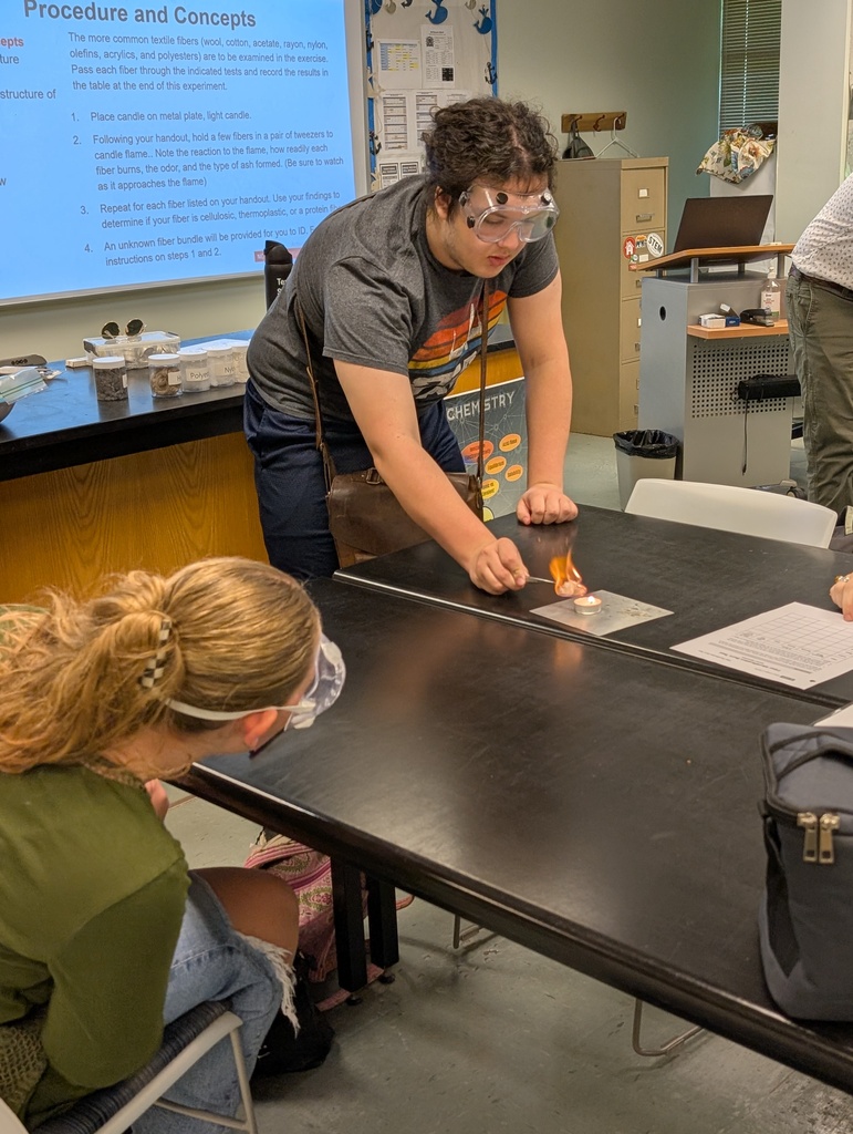Student lighting cotton on fire over candle while group mate watches intently