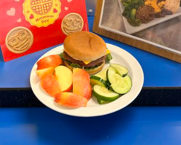 Cheesburger on plate with apples and cucumbers. 