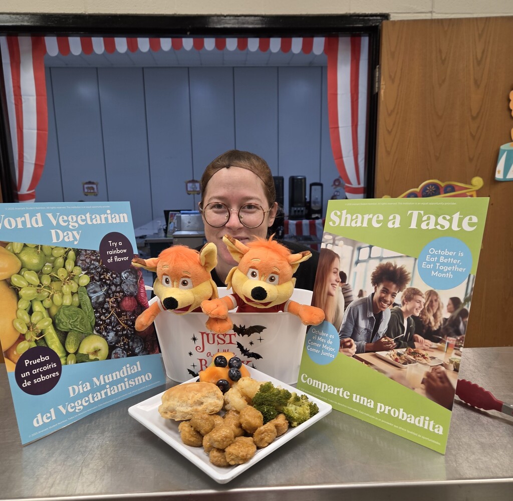 Child Nutrition staff smiling behind display plate of popcorn chicken, biscuit, broccoli, and fruit