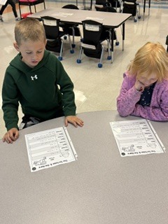 first grade students working in pairs on a readers theater assignment