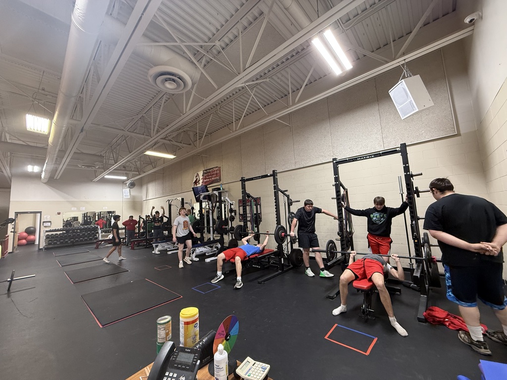 Students doing bench press in groups, 6 benches one student on each bench with spotters 