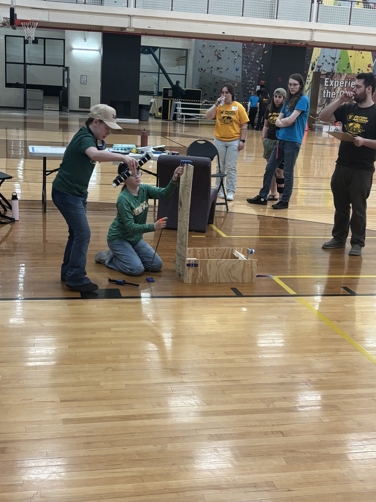 Students competing in Math Olympiad, building their project, a wood structure, as judges and other students watch.