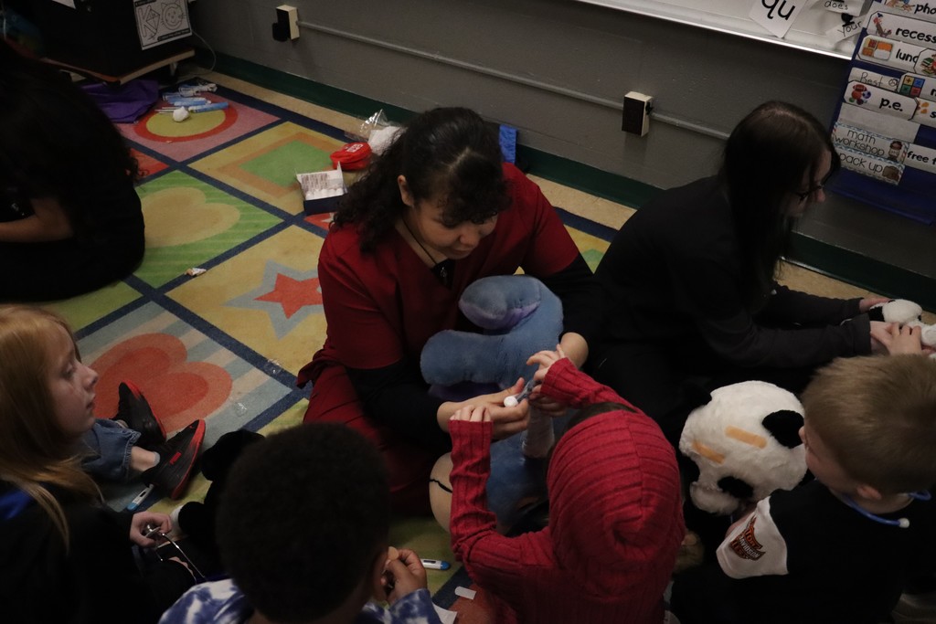 Students and nurse wrapping a stuffed animal arms with gauze
