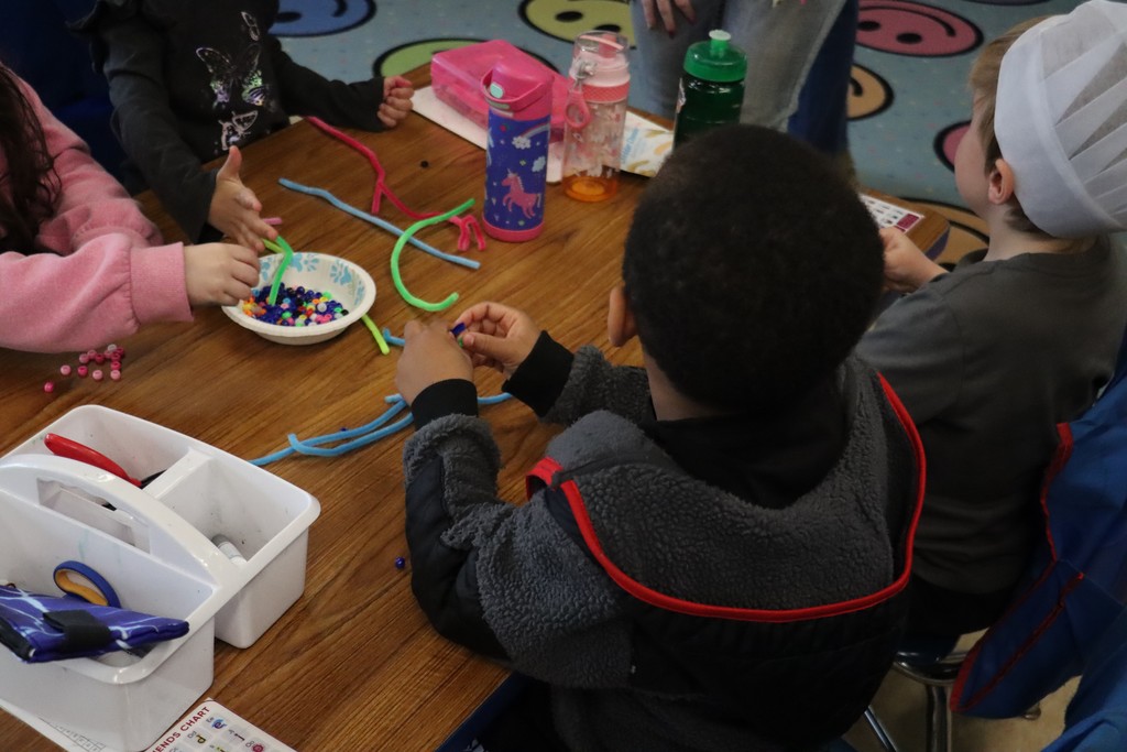 Students sitting around table playing with pipe cleaners and beads