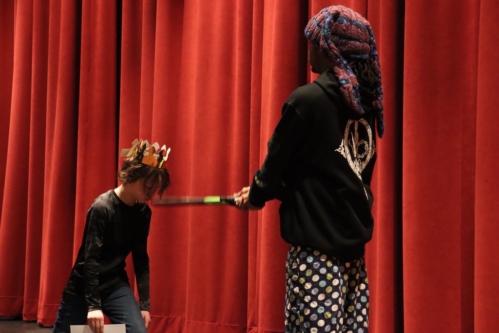 Student being "knighted" with fake sword on stage by teacher