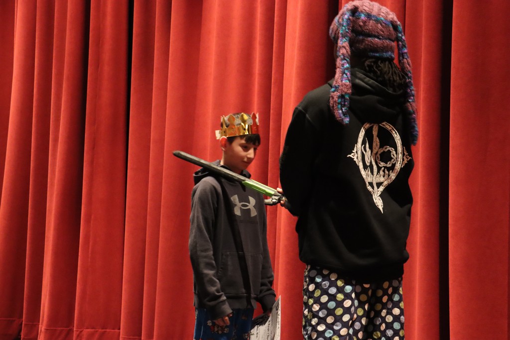 Student being "knighted" with fake sword on stage by teacher