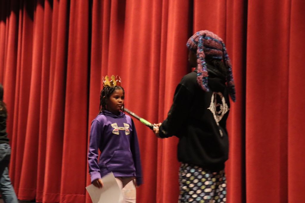 Student being "knighted" with fake sword on stage by teacher