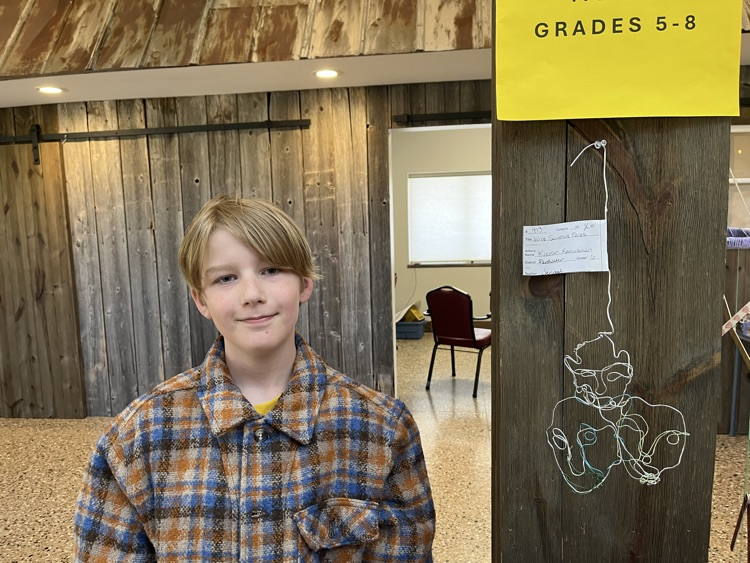 Kieran stands in front of his wire sculpture. 