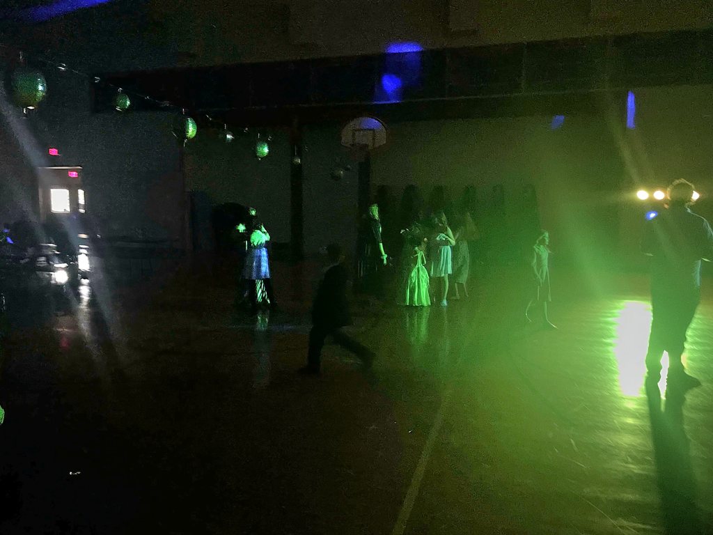 Elementary kids and their families dancing in a dark gym.